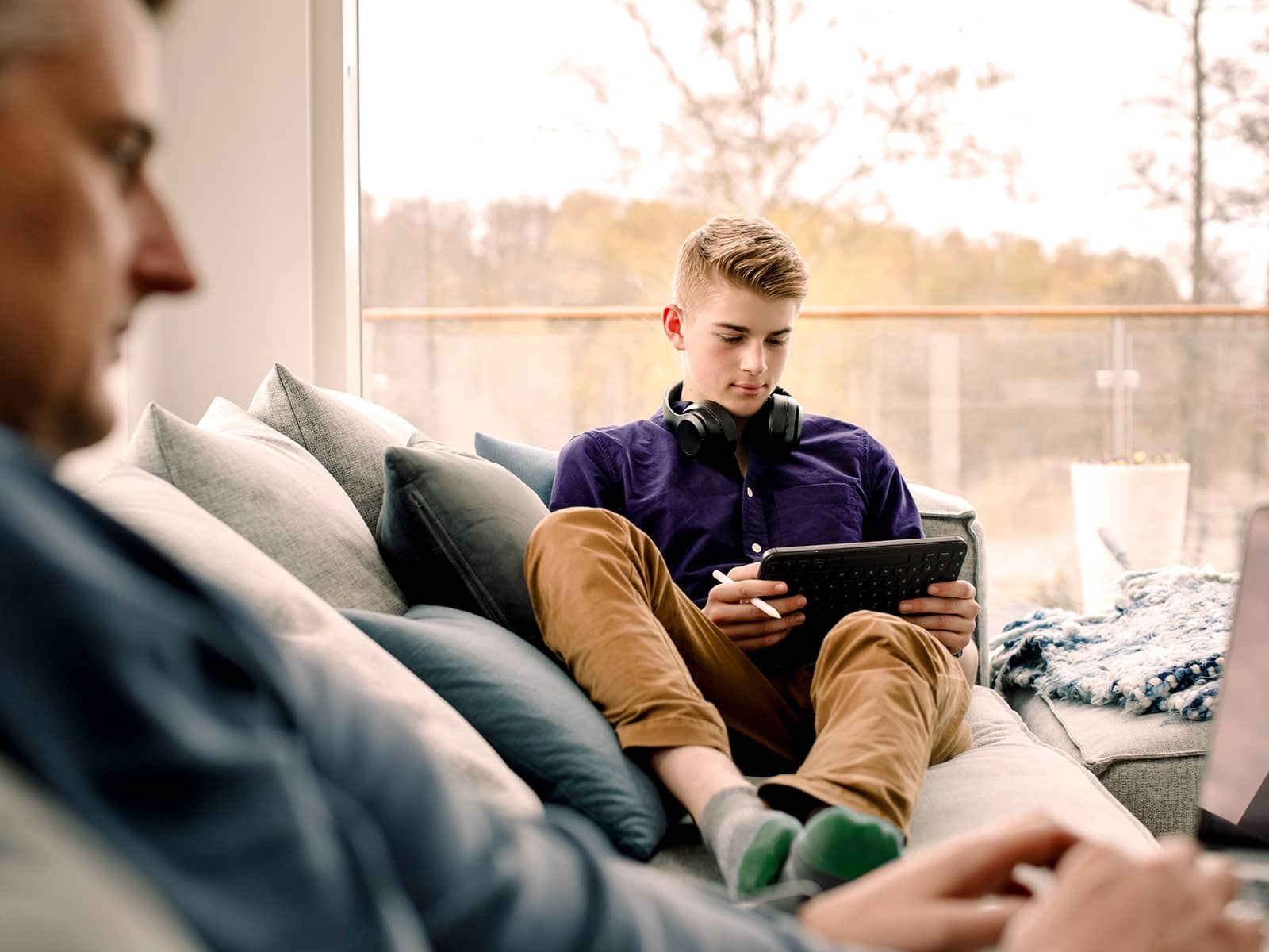 Teenagedreng sidder med tablet i sofa, hvor han bestiller fiberbredbånd. Med fiber fra EWII får han hurtigt og stabilt bredbånd uden binding. Bestil fiberbredbånd her.