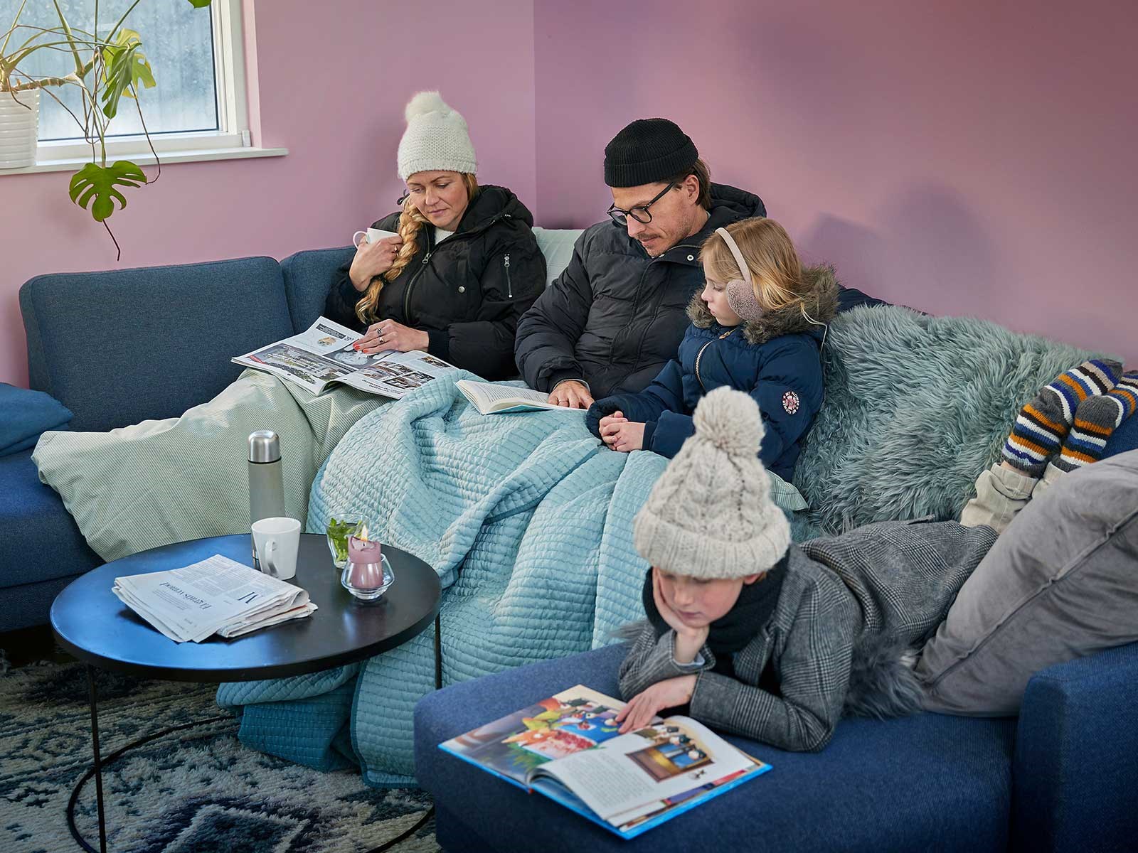 Familie sidder i sofa med vintertøj på. De fryser, fordi de ikke har en varmepumpe. Se hvad koster en varmepumpe på abonnement her.