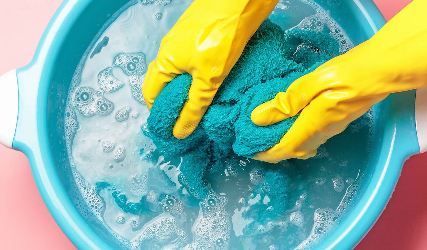Et par gule gummihandsker der er ved at vaske et håndklæde i en turkis balje med vand. Hvilke vaskeprogrammer på din vaskemaskine er bedst og hvor meget strøm bruger en vaskemaskine?